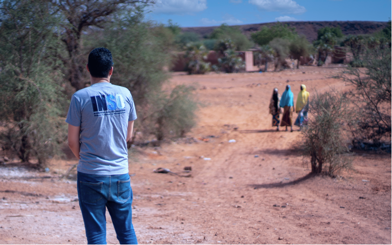 INSO staff in Niger, looking out to red dirt and three women in the distance