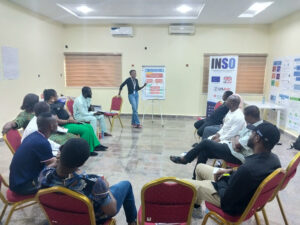 A group of participants sat on chairs in a circle whilst the trainer points to a flipchart.